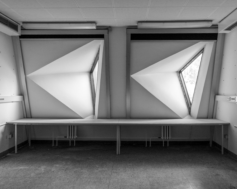 Innenraum im Mäusebunker Berlin: zwei trichterförmige Dreiecksfenster über einer durchlaufenden Laborbank, strenge geometrische Betonarchitektur der Hänskas in Schwarzweiß